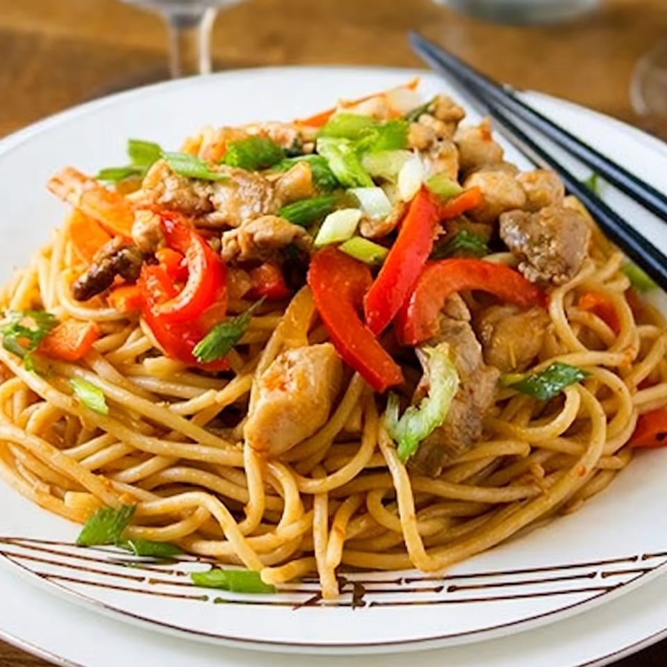 Chicken lo mein with red bell peppers and green onions on a white plate with chopsticks.