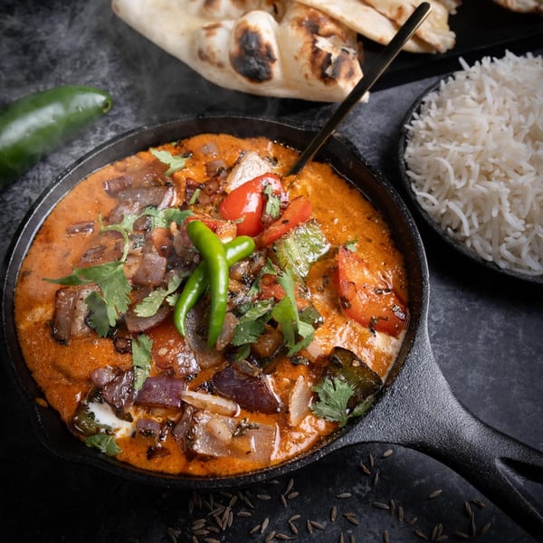 Steaming Indian curry with vegetables, cilantro, and chili peppers, served with rice and naan.