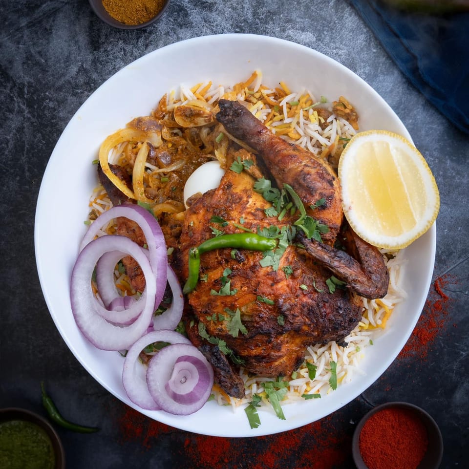 Indian chicken biryani with roasted chicken, rice, onions, lemon, and green chili.