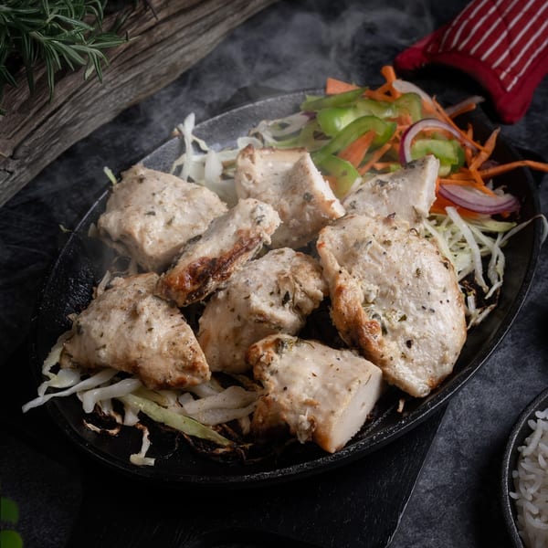 Steaming hot Indian chicken tikka pieces with cabbage and salad on a black platter.