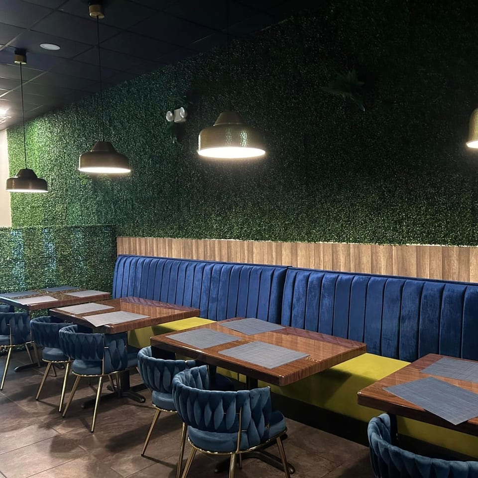 Interior of Red Chillez Indian Cuisine with blue velvet booths, wooden tables, and a green wall.