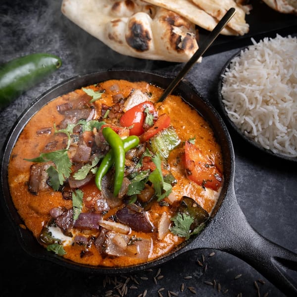 Steaming Indian curry with vegetables and cream in a cast iron pan, with naan and rice.