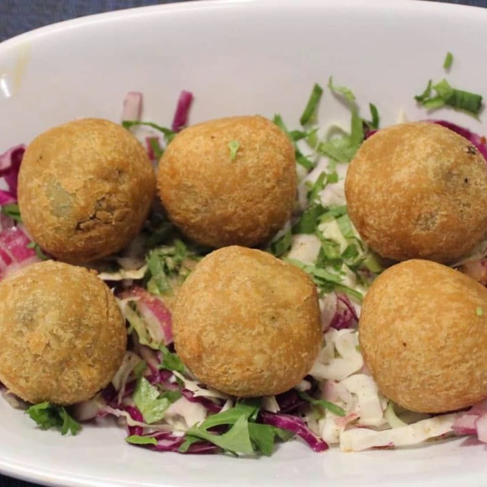 Six golden-brown Indian fried potato balls, or aloo bonda, served on a bed of shredded cabbage and red onion.