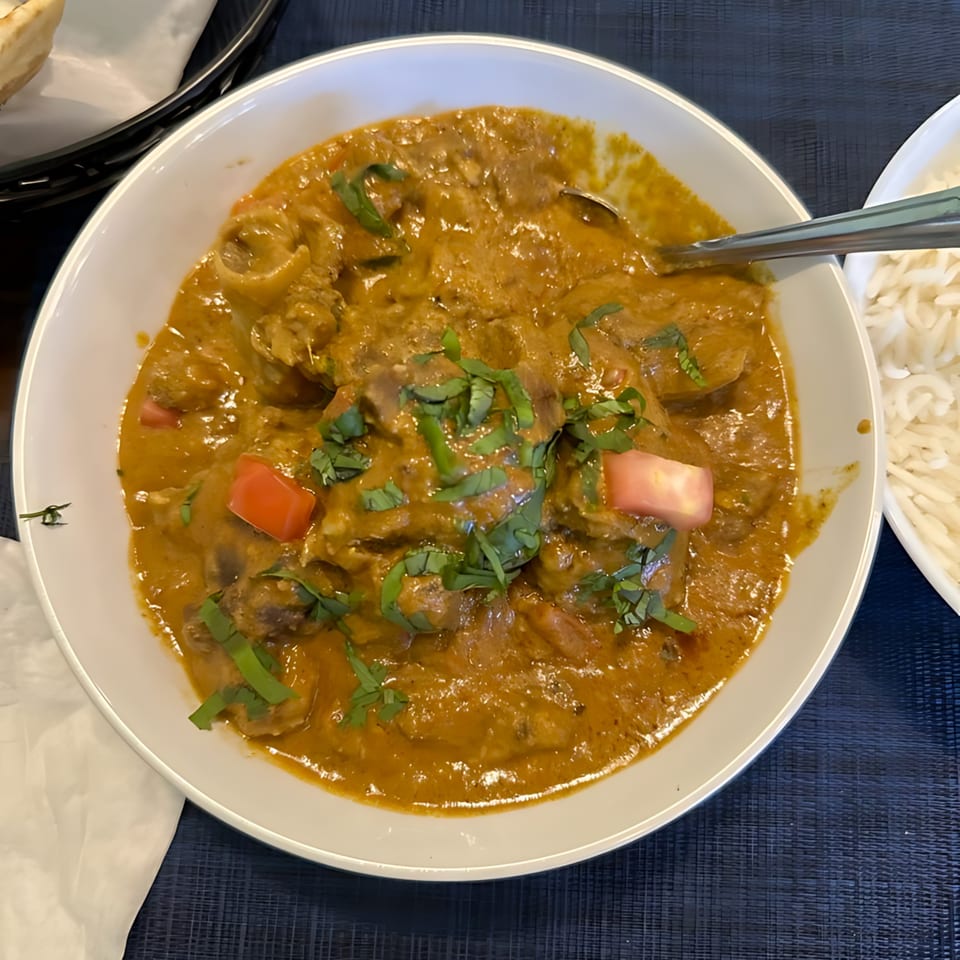 A bowl of Indian curry with meat, red peppers, and fresh herbs, served with rice.