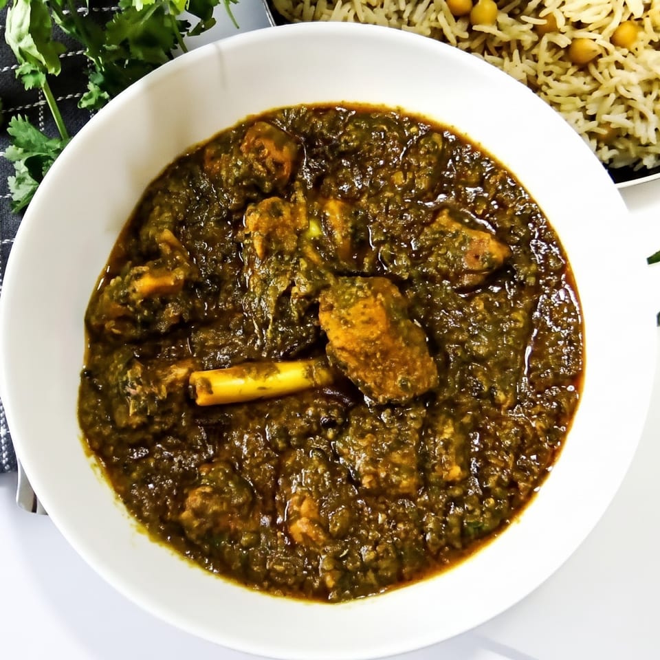A white bowl filled with green chicken curry, served with rice and chickpeas.