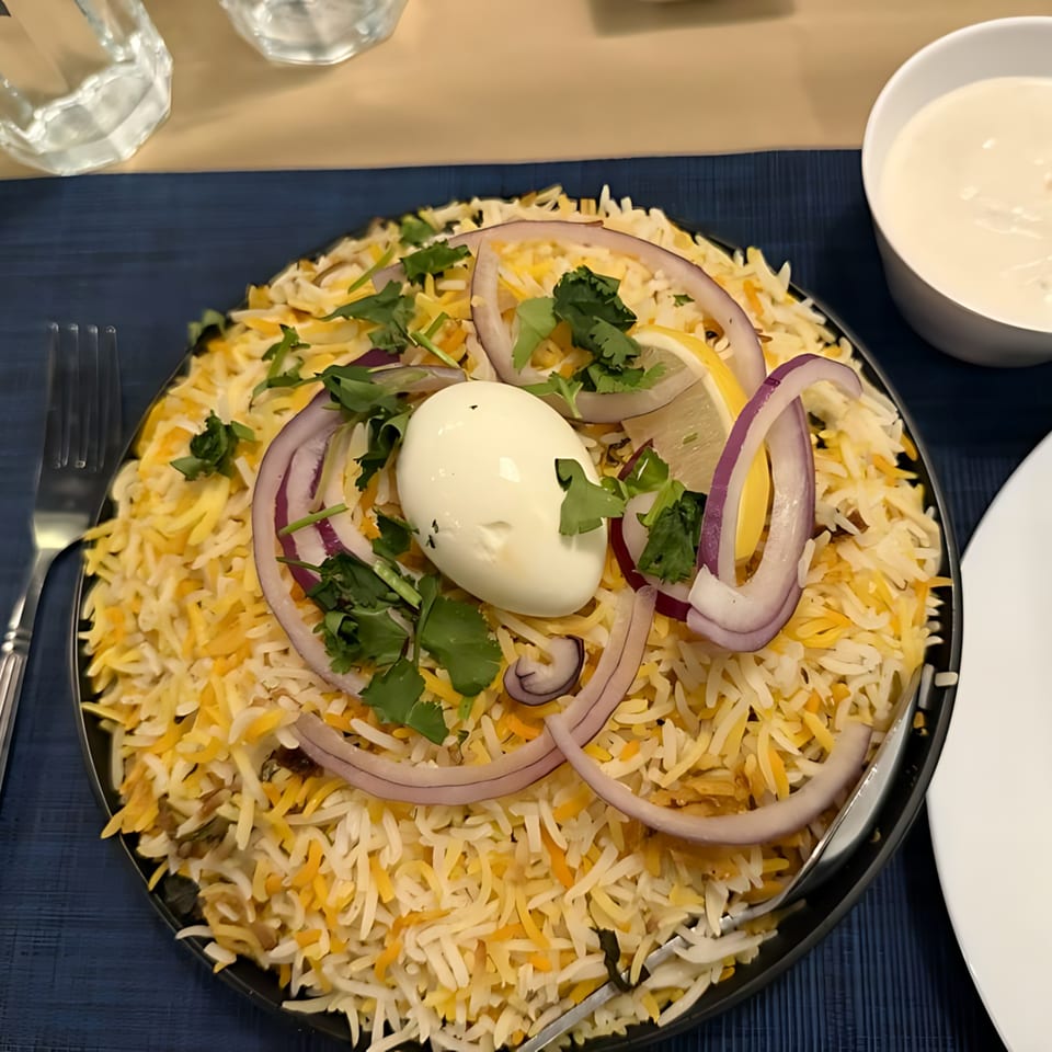 Indian biryani with rice, egg, red onion, cilantro, and lemon, served with raita.