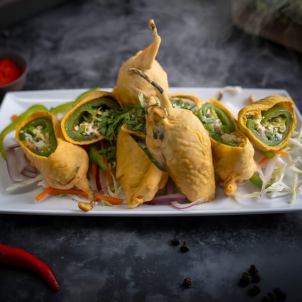 Red Chillez Indian Cuisine's chili pakora, deep-fried chili peppers stuffed with spices, served on a white plate.