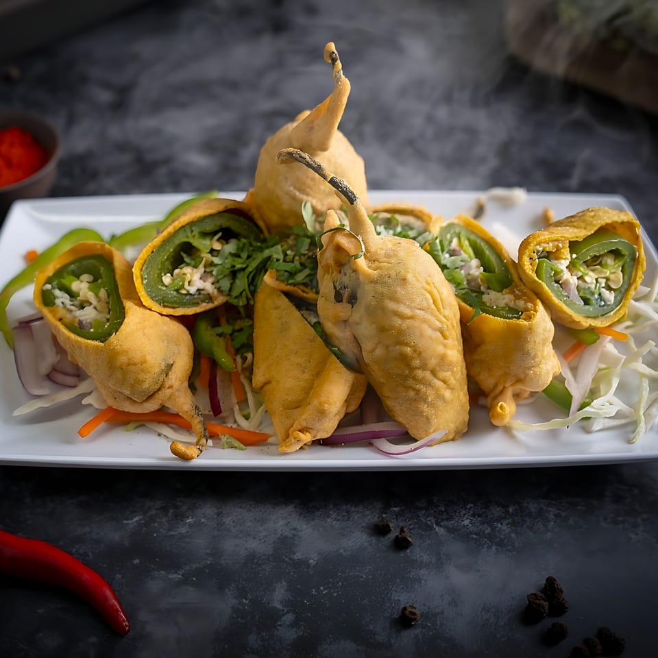 Red Chillez Indian Cuisine's chili pakora, deep-fried chili peppers stuffed with spices, served on a white plate.