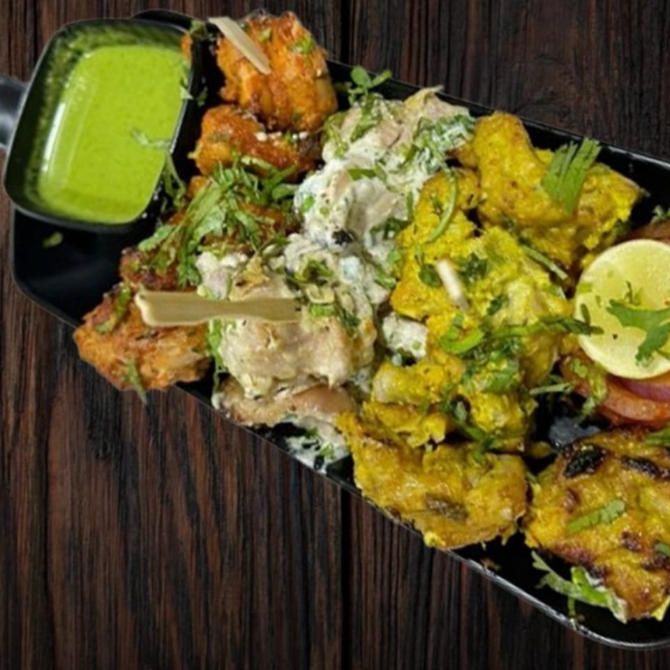A platter of various Indian chicken dishes, including tandoori, malai, and hariyali, with green chutney.