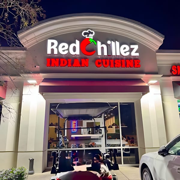 The illuminated Red Chillez Indian Cuisine restaurant sign at night, with a golf cart and car parked outside.